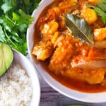 Bacalao a la Vizcaina served in a white bowl with a side of white rice, half of an avocado and cilantro.