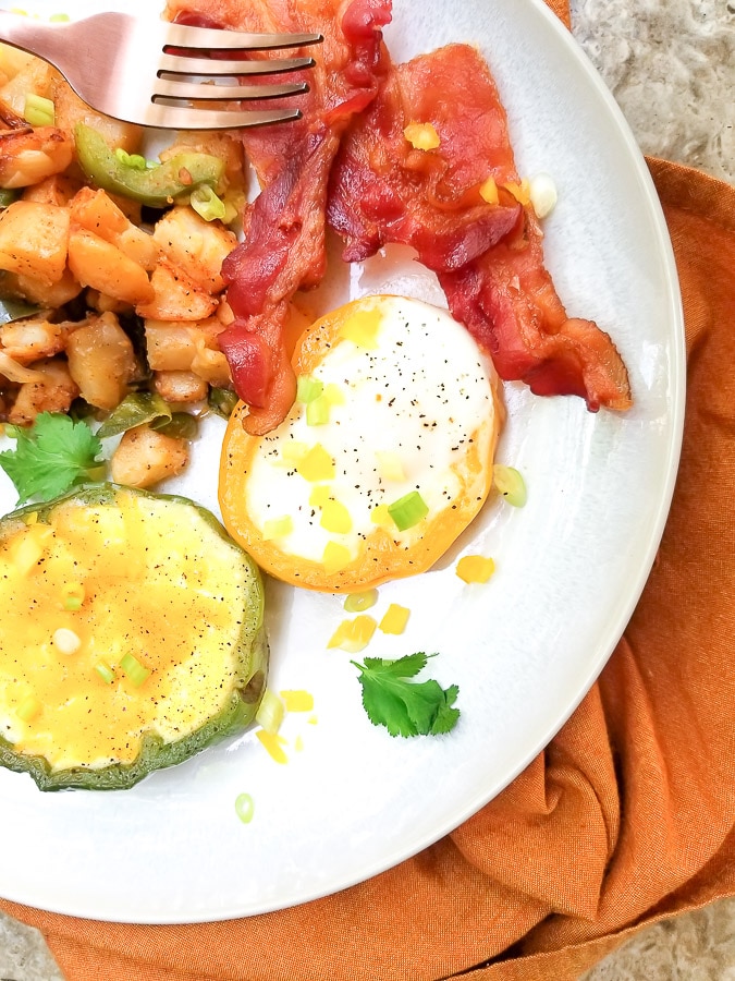 Bell Pepper Eggs with home fries, sausage and bacon served on a white plate.