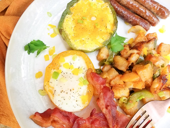 Bell Pepper Eggs with home fries, sausage and bacon served on a white plate.