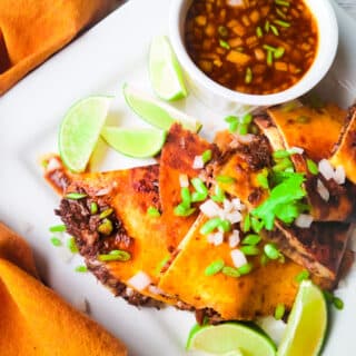 Birria Quesadillas served on a what platter with consomme and lime wedges.