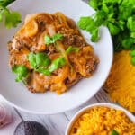 Bistec en Salsa (Cube Steaks in Tomato Sauce) serve in a white bowl with a side of yellow rice with corn and avocado.