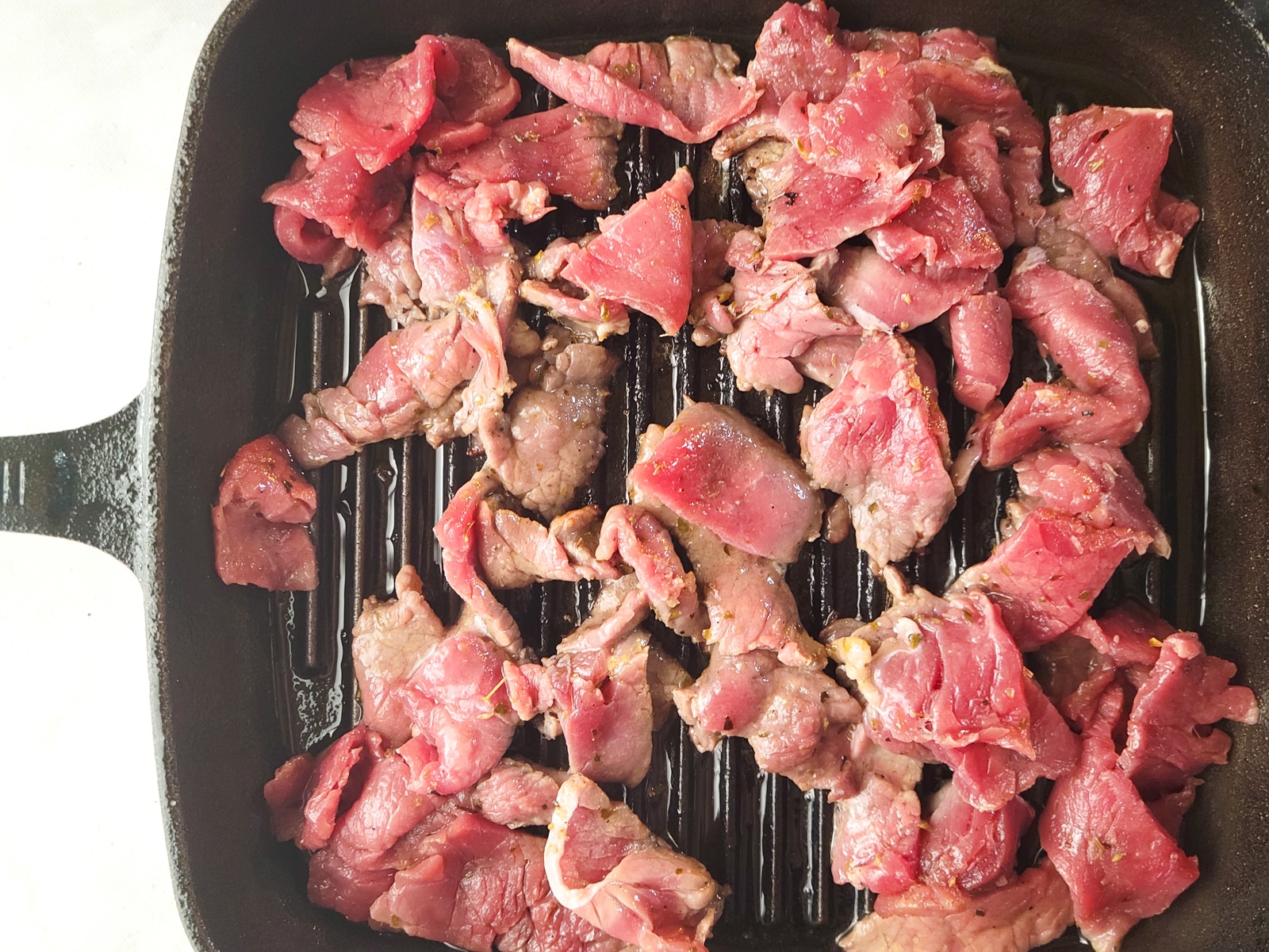 Pieces of steak cooking in a cast iron skillet.