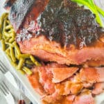 A fully cooked Bourbon Maple Glazed Ham served on a large white platter with a side of green beans.