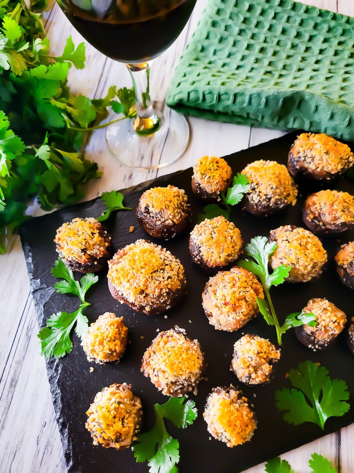 Boursin stuffed mushrooms served on black slate with a glass of red wine beside it.