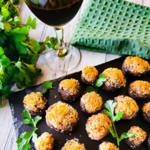 Boursin stuffed mushrooms served on black slate with a glass of red wine beside it.