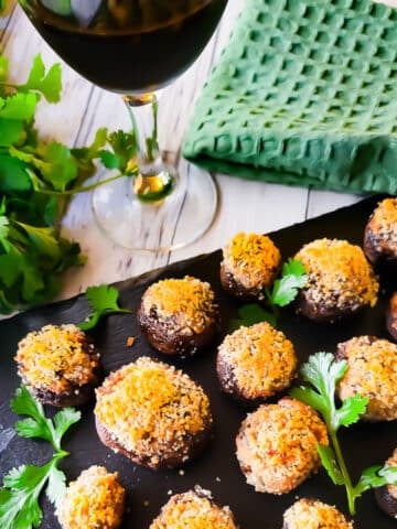 Boursin stuffed mushrooms served on black slate with a glass of red wine beside it.