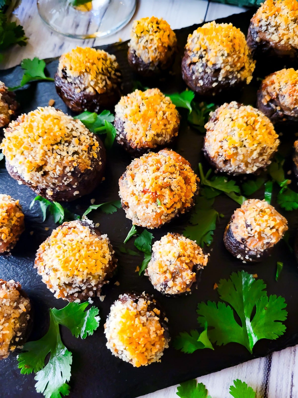 Boursin stuffed mushrooms served on black slate with a glass of red wine beside it.