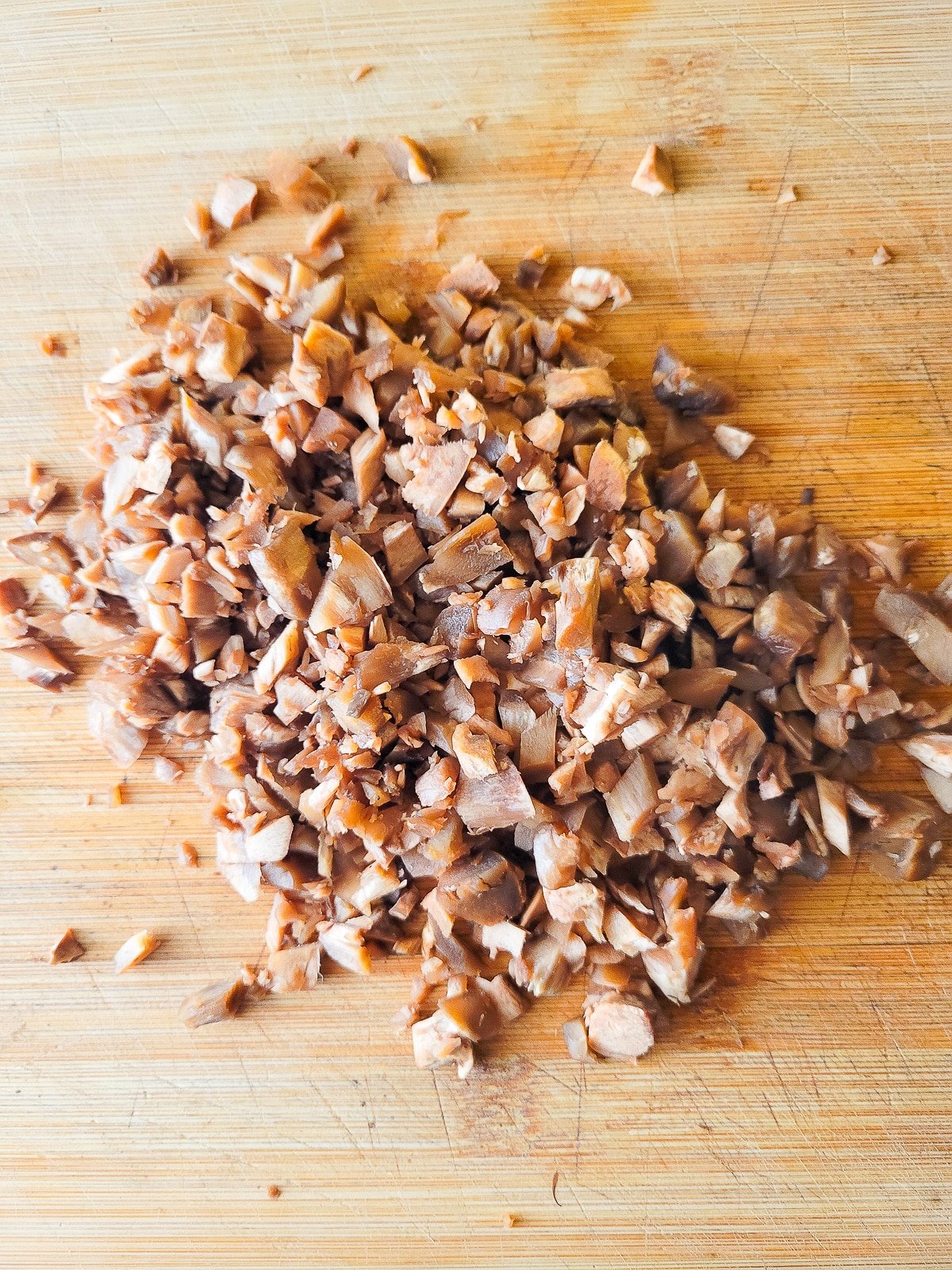 Finely chopped baby bella stems on a wooden cutting board.
