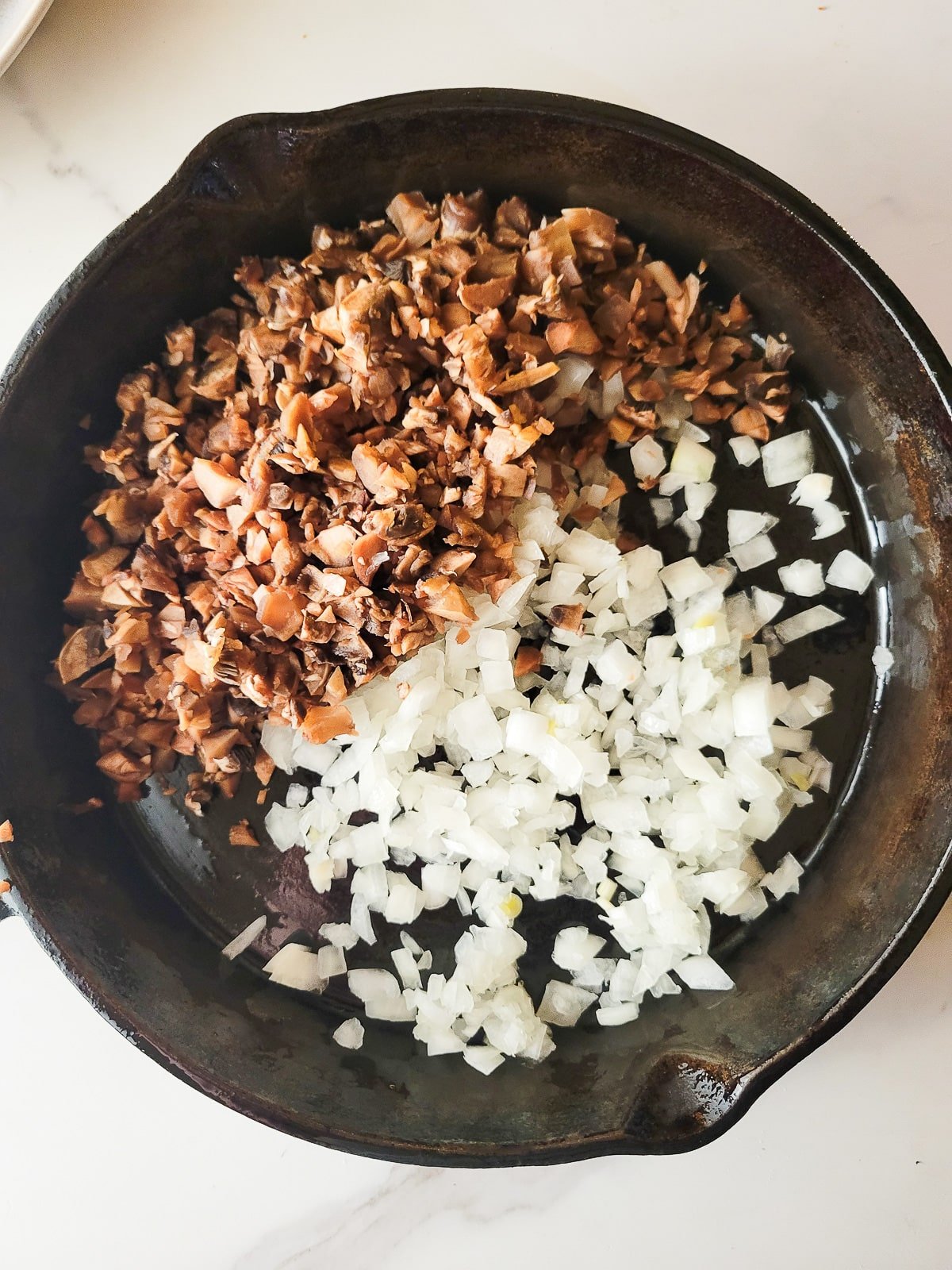 The chopped mushroom stems and onions added to a cast iron skillet.