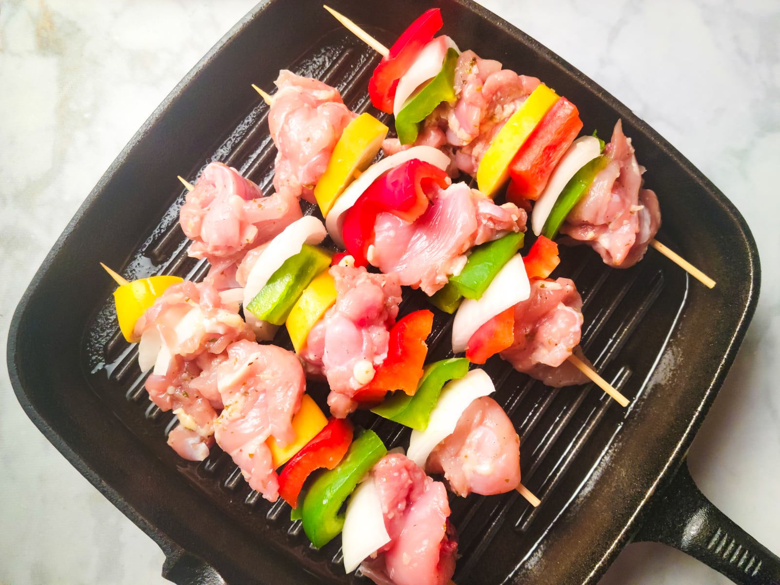 Brochetas de pollo sitting in a cast iron grill skillet, about to cook.