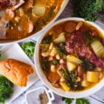 Caldo Gallego (Galician Broth) served in a white bowl with a side of crusty bread and a whole pot of cooked soup beside it.
