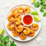 Camarones coco (coconut shrimp) served on a white round plate with chili duck sauce and lime wedges.