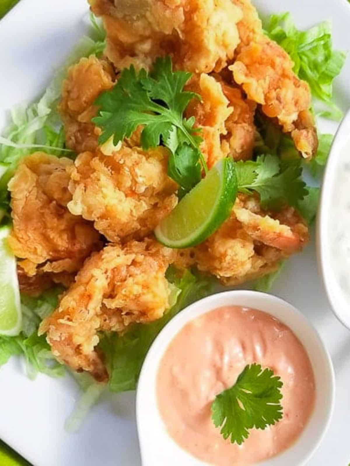 Camarones empanizados (battered shrimp) served with jalapeno mayo sauce, mayo-ketchup with lime wedges on a white platter.