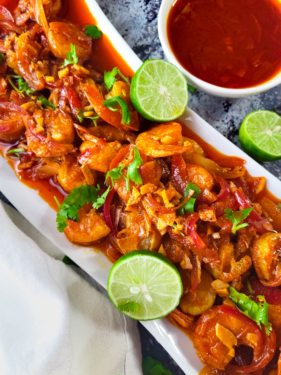Camarones a la Cucaracha (Spicy Fried Shrimps) served on a white platter with lime wedges.