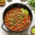 Carne deshebrada cooked in a cast iron pot with small condiment bowls around it.