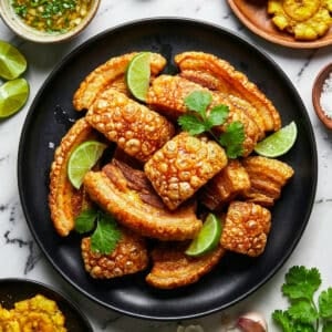 Chicharrones de cerdo served on a black plate, topped with lime wedges.