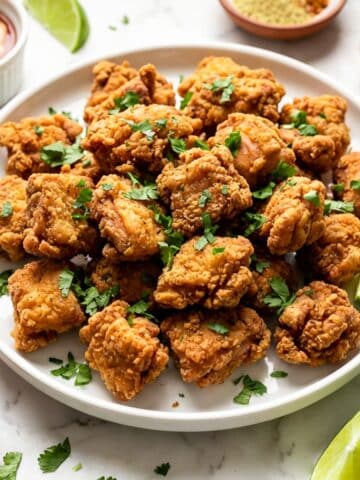 Puerto Rican chicharrones de pollo served on a white platter with lime wedges with a side of mayoketchup.