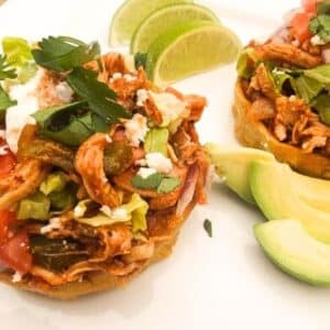 Chicken Sopes with all the toppings! Avocado, queso fresco, tomatoes, onions, salsa verde and red sauce served on a white platter.