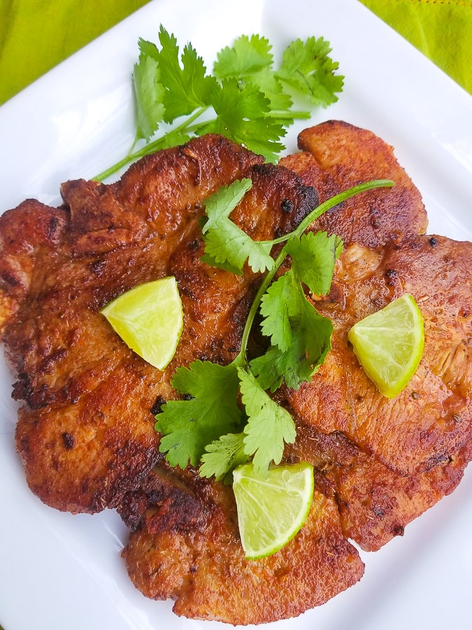 Puerto Rican Fried Pork Chops served on a white platter and topped with lime wedges.
