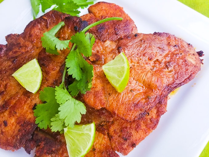 Puerto Rican Fried Pork Chops served on a white platter and topped with lime wedges.