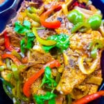 Chuletas Guisadas (Puerto Rican Stewed Pork Chops) cooked in a cast iron skillet, covered with onions, peppers and cilantro sprigs.