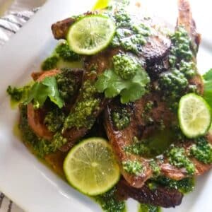 Chuletas con Salsa de Cilantro (Pork Chops with Cilantro Sauce) served on a white platter and topped with slices of lime.