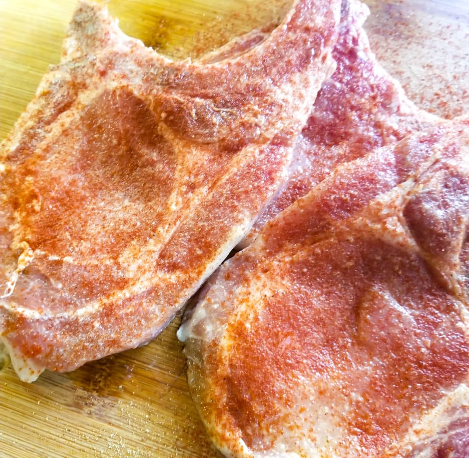 Seasoned pork chops on a wooden cutting board.