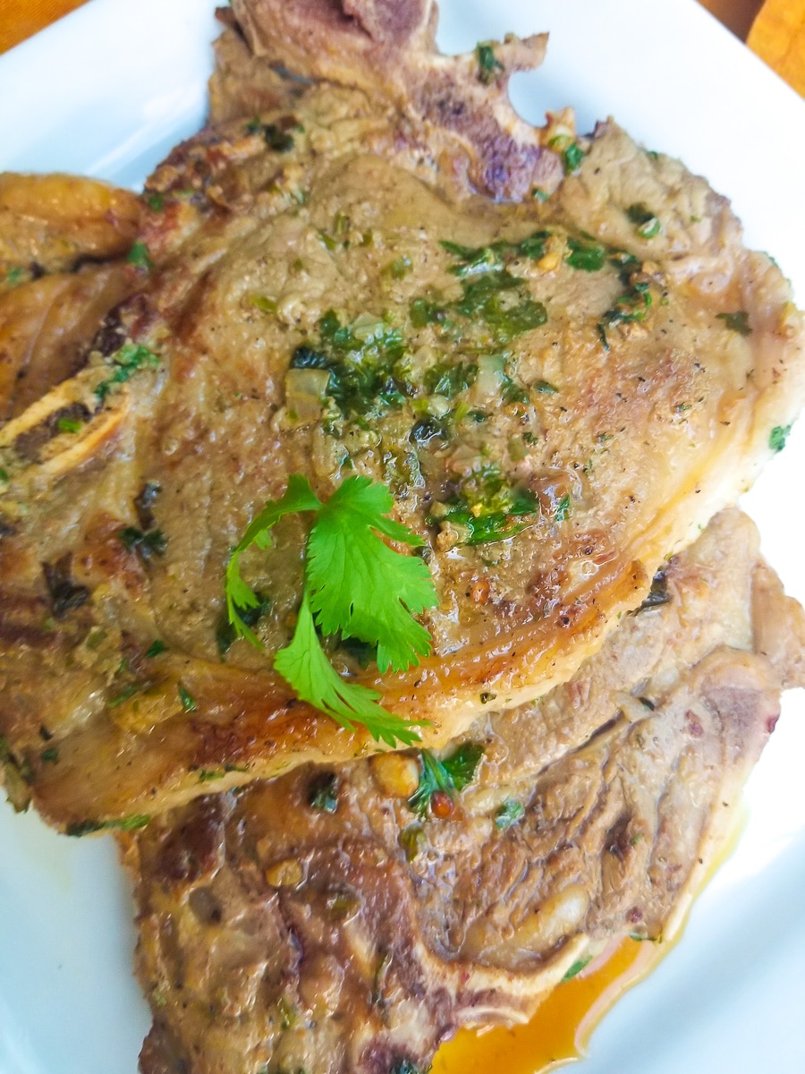 Chuleton a la plancha (Ribeye Steak) served on a white platter and topped with cilantro sprigs for garnish.