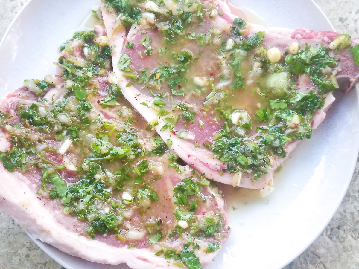 Rib eye steaks on a plate topped with chimichurri sauce to marinade.