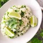 Cilantro Lime Rice (Arroz con Cilantro) served in a white bowl and topped with extra cilantro and lime wedges.