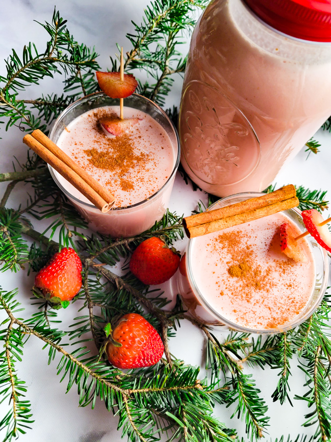 Coquito de Fresa (Strawberry Coquito) served in two glass cups displayed on top of marble background with whole strawberries and cinnamon sticks.