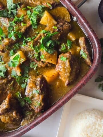 Costillas en salsa verde cooked in a large saucepan with a side of white rice and avocado.