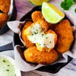 Fried Crab Croquettes (croquetas de cangrejo) in a small cast iron pan with a side of horseradish dipping sauce and lime wedges.