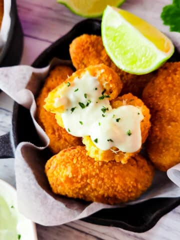 Fried Crab Croquettes (croquetas de cangrejo) in a small cast iron pan with a side of horseradish dipping sauce and lime wedges.