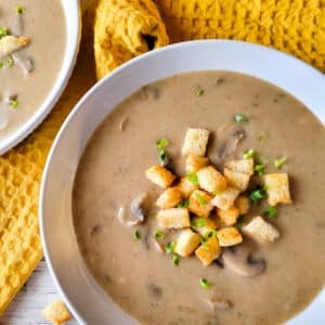 Crema de hongos, (cream of mushroom soup) in a white bowl topped with chopped scallions.