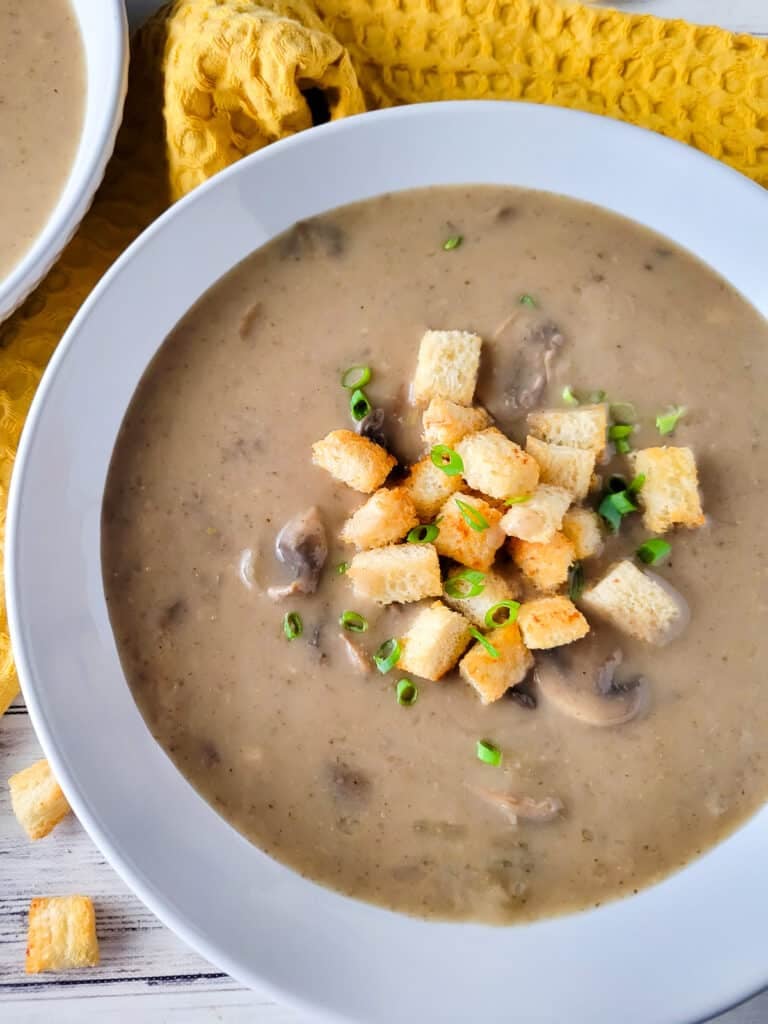 Crema de hongos, (cream of mushroom soup) in a white bowl topped with chopped scallions.