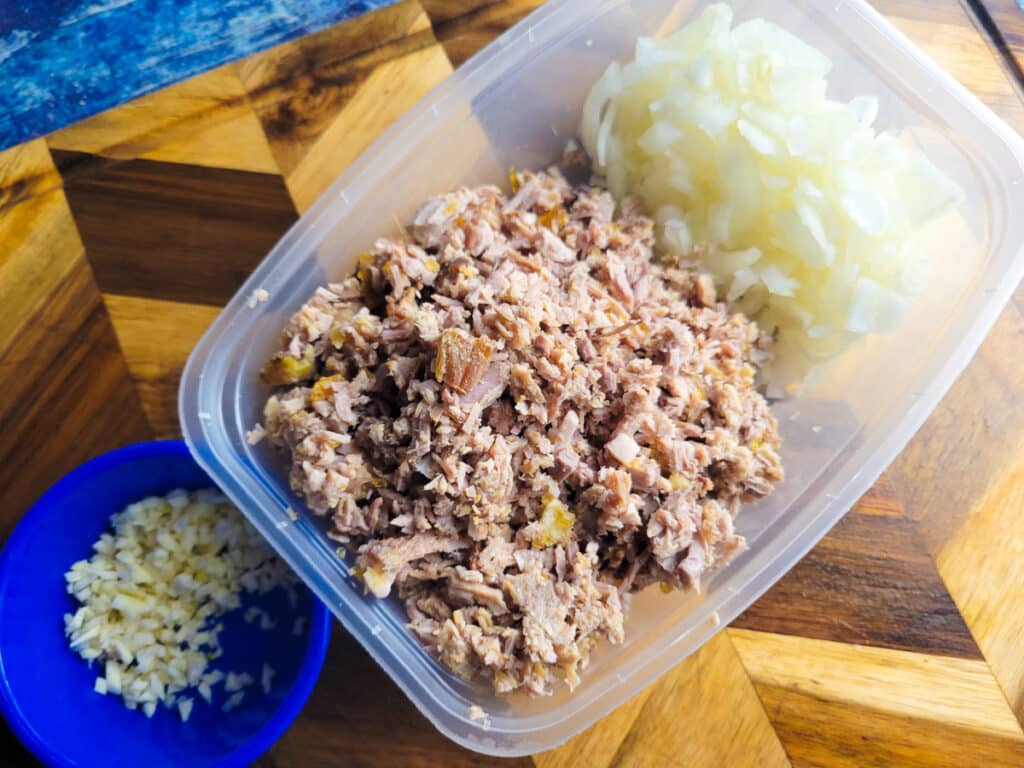 Chopped garlic, pork and onions in separate containers sitting on top of a wooden cutting board.