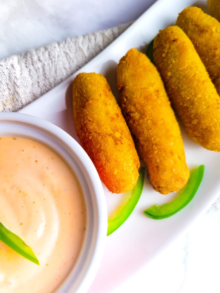 Cuban Croquetas (Cuban Croquettes) served on a white platter with a creamy mayoketchop sauce on the side.