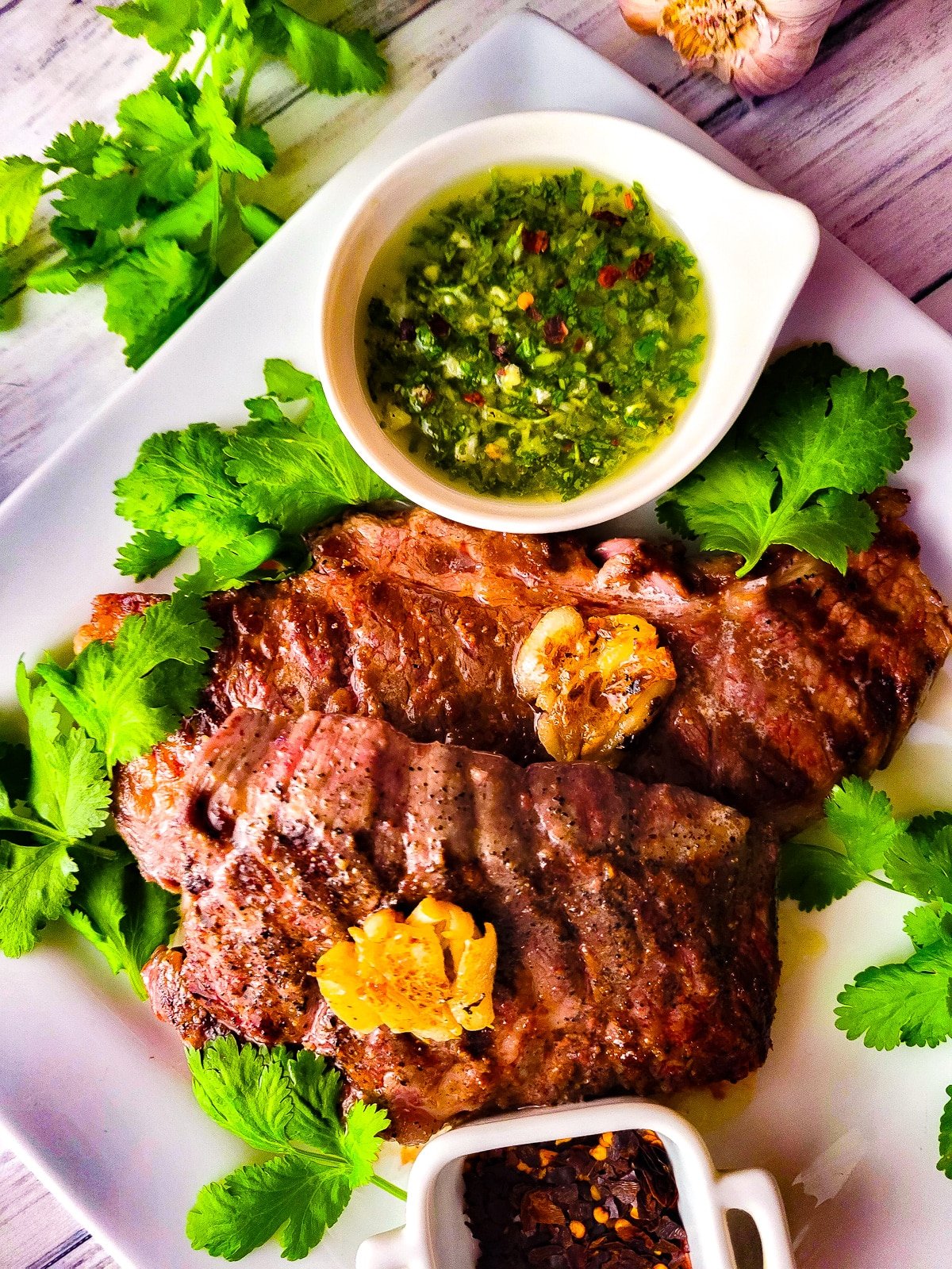 Denver steaks served on a white platter with a side of chimichurri sauce.