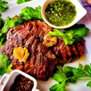 Denver steaks served on a white platter with a side of chimichurri sauce.