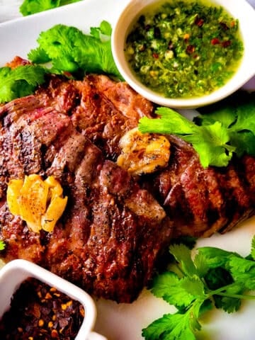 Denver steaks served on a white platter with a side of chimichurri sauce.