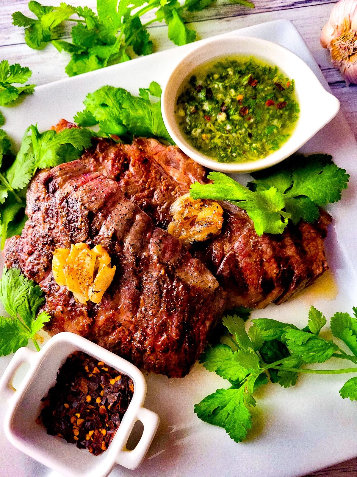Denver steaks served on a white platter with a side of chimichurri sauce.