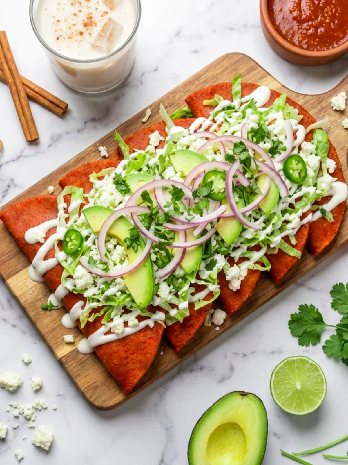 Enchiladas Potosinas served on a wooden cutting board, topped with shredded lettuce, avocado, red onions, and jalapenos. Beside it, a glass of Mexican horchata and avocado.