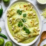 Chicken enchiladas suizas served on a white platter, topped with sliced onions and chopped cilantro.