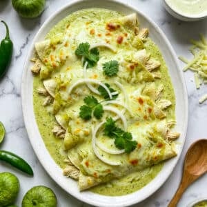 Chicken enchiladas suizas served on a white platter, topped with sliced onions and chopped cilantro.