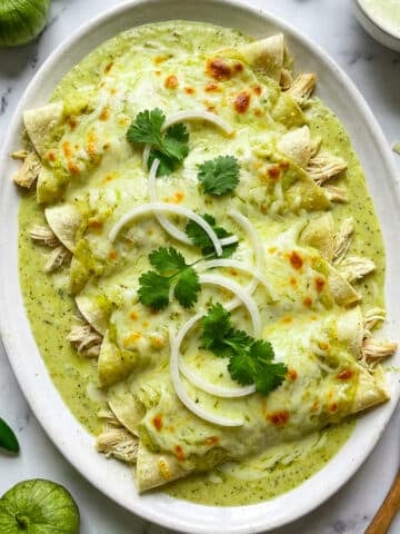 Chicken enchiladas suizas served on a white platter, topped with sliced onions and chopped cilantro.