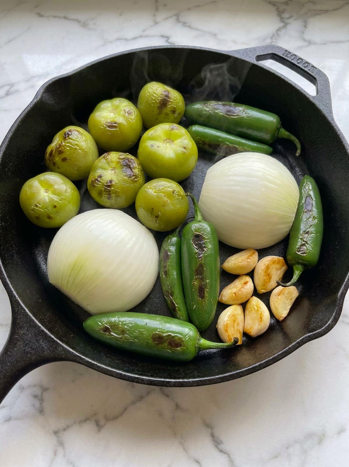 Roasting tomatillos, jalapenos, garlic and onions in a cast iron skillet to make salsa verde.