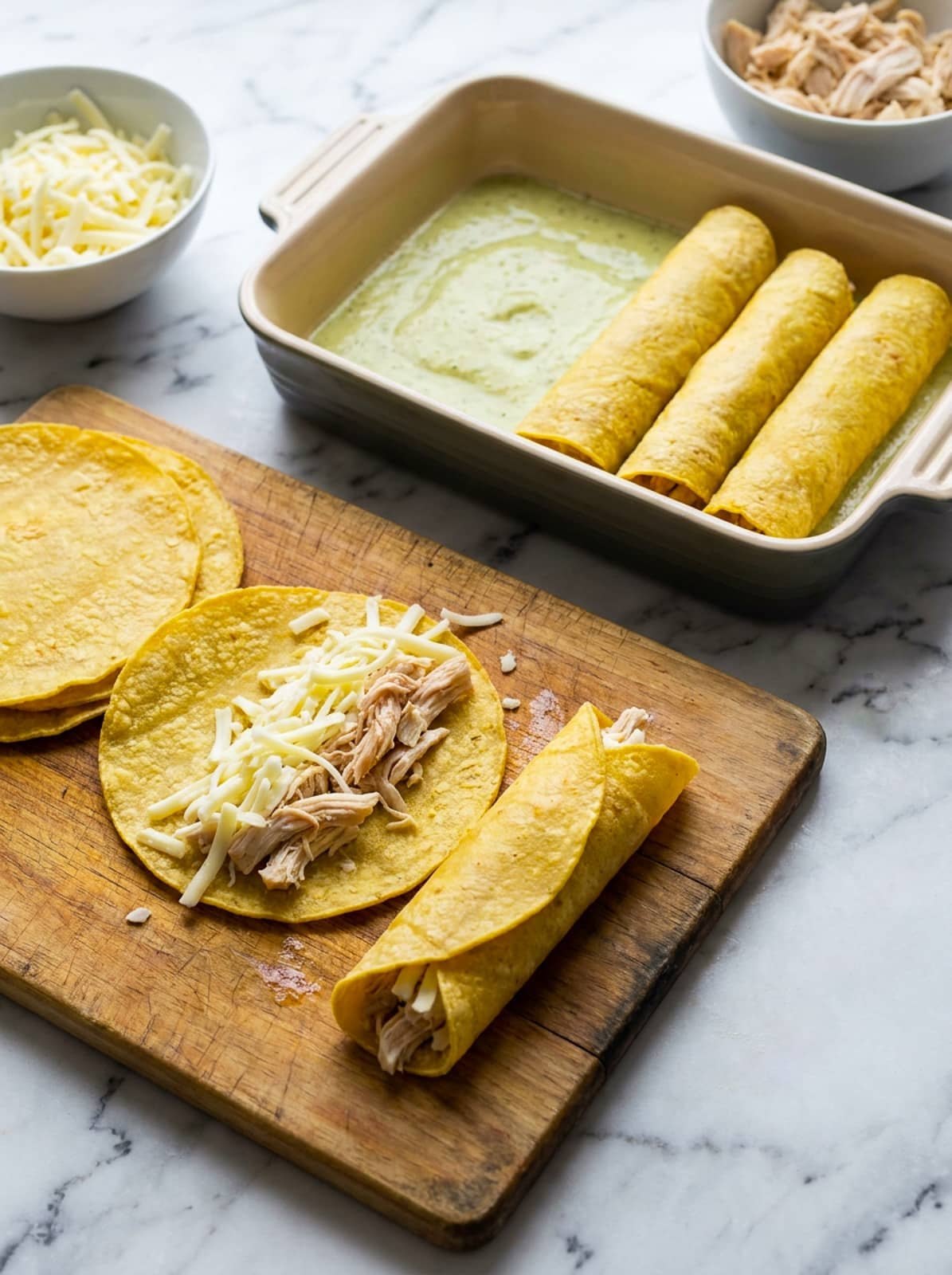 Assembling the enchiladas with the chicken and cheese and adding them to a ceramic casserole.