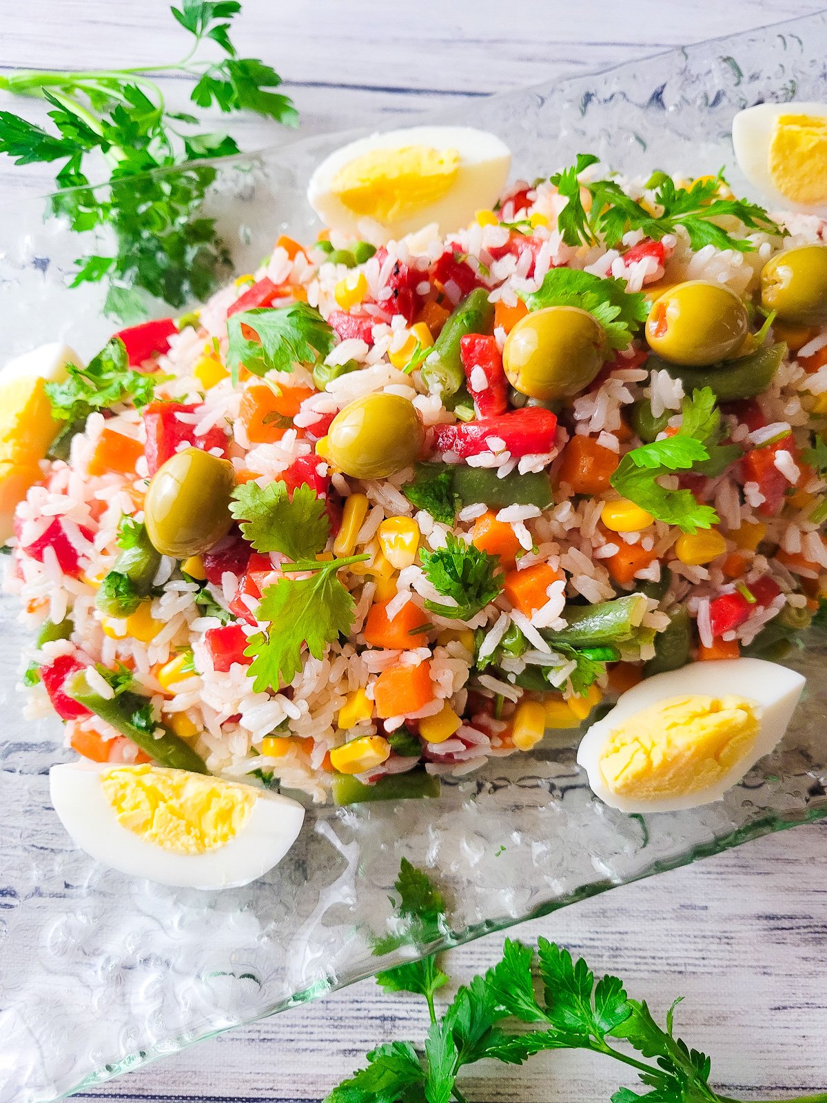 Ensalada de Arroz Primavera (Garden Rice Salad) served on a transparent serving platter, topped with olives and hard boiled eggs sliced.