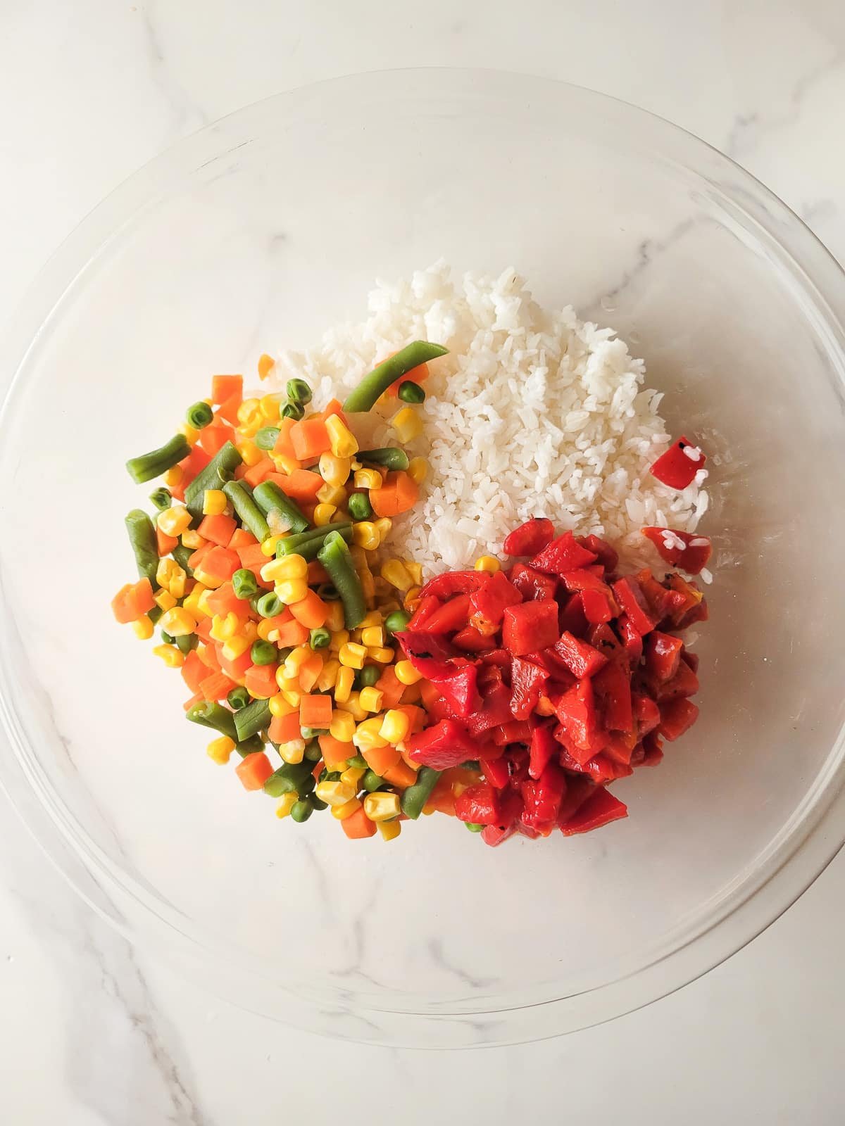 Rice, roasted bell peppers and vegetables in a mixing bowl.